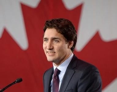 Justin Trudeau przemawiający dynamicznie z mównicy podczas wiecu politycznego lub konferencji prasowej, z tłem sugerującym publiczne wydarzenie.