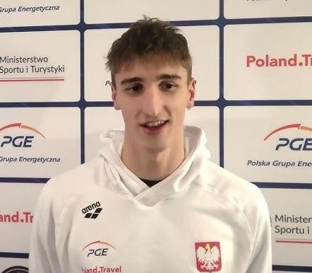Ksawery Masiuk podczas dynamicznego wyścigu pływackiego stylem grzbietowym, otoczony rozbryzgującą się wodą, ukazujący siłę i technikę.