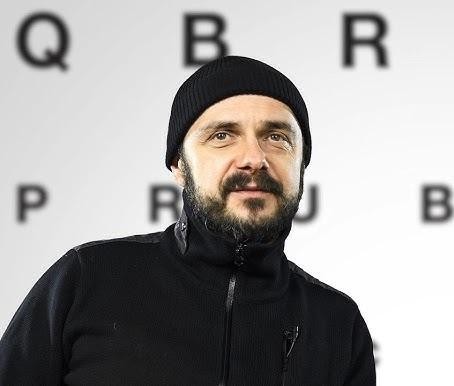 Arkadiusz Jakubik, wokalista zespołu Dr Misio, śpiewający z pasją do mikrofonu na scenie podczas koncertu. Dynamiczne ujęcie z nastrojowym oświetleniem scenicznym.