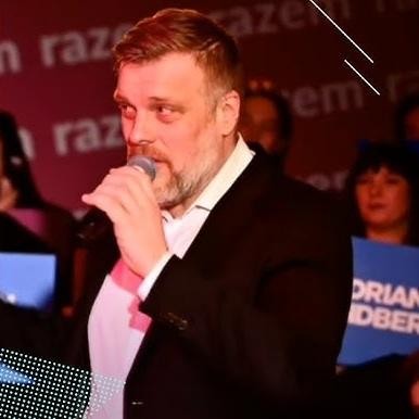Adrian Zandberg z rodziną w domowym otoczeniu, uśmiechnięty, w otoczeniu żony Barbary i dzieci Olgi i Olafa, symbolizujący wsparcie rodzinne.