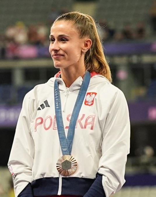 Natalia Bukowiecka na bieżni, celebrująca zwycięstwo z uniesionymi ramionami i szerokim uśmiechem.