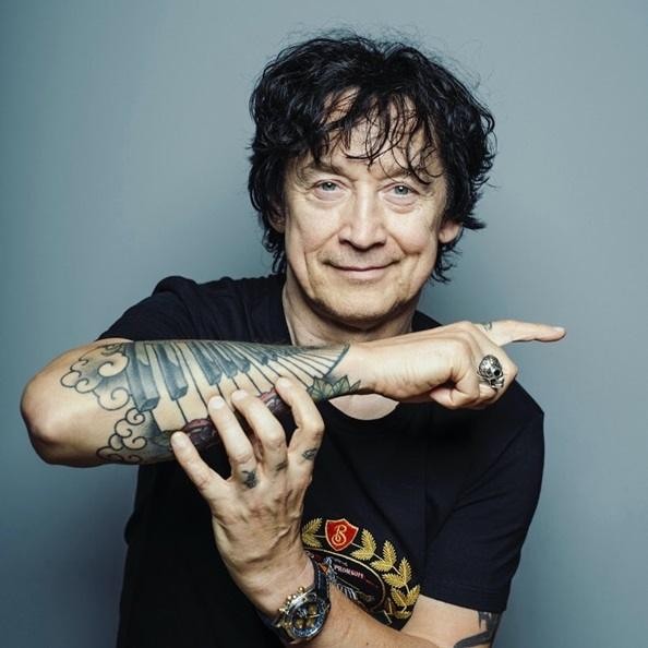 Jan Borysewicz grający na gitarze elektrycznej podczas koncertu, z widocznym skupieniem i energią sceniczną.