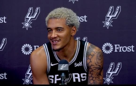 Jeremy Sochan w koszulce San Antonio Spurs, z determinowanym wyrazem twarzy, na boisku koszykarskim.
