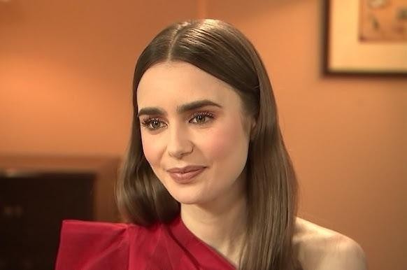 Lily Collins uśmiechnięta na planie filmowym, w tle delikatnie widoczne rekwizyty filmowe.
